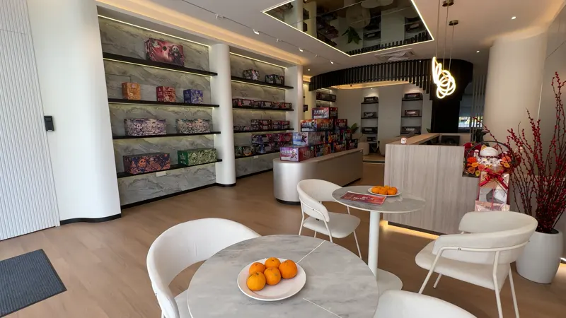 A round table with a bowl of oranges and white chairs, set beside the product wall for working an order out.